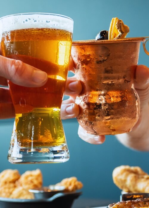 Two people clinking beer glass and copper mug with orange and cherry